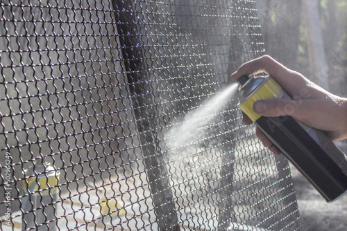 Spray can with paint in hand. Black paint is sprayed from the spray can on the metal net. Workman working with paint painting