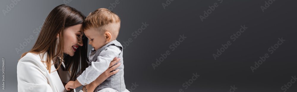 happy young woman smiling near little son on grey with copy space, banner. happy young woman smiling near little son on grey with copy space, banner.