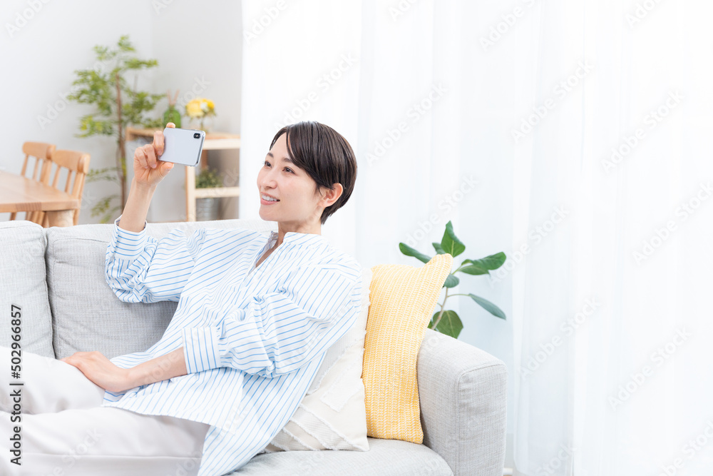 ソファーに座るミドル女性（スマホ・横向き・インターネット・動画鑑賞）