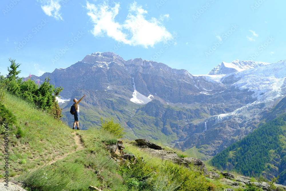 young tourist with backpack, man stands on mountain, Swiss Alps with snow-capped Matterhorn peak visible in background, concept of hiking, rock climbing, active lifestyle, beauty of nature