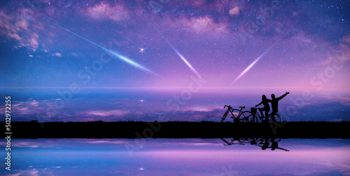 meteorites fly in the night sky. Silhouette Couple cycling on Panorama blue night sky milky way and star on dark background.Universe filled with stars, nebula and galaxy with noise and grain.