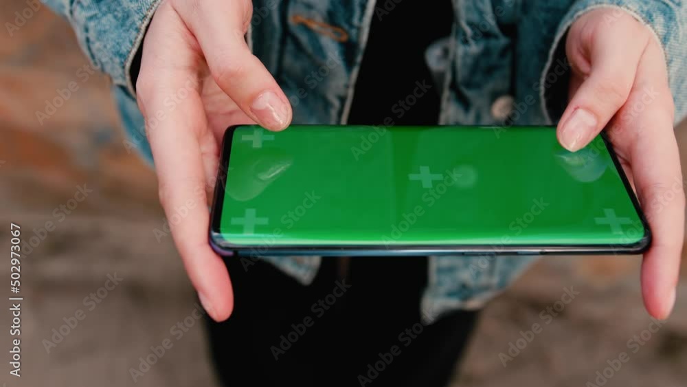 Woman uses a phone with a green screen layout, a color key, Watching content, Videos, photos, playing a game. Use green screen for copy space closeup. Chroma key mock-up on smartphone in hand. Woman uses a phone with a green screen layout, a color key, Watching content, Videos, photos, playing a game. Use green screen for copy space closeup. Chroma key mock-up on smartphone in hand.