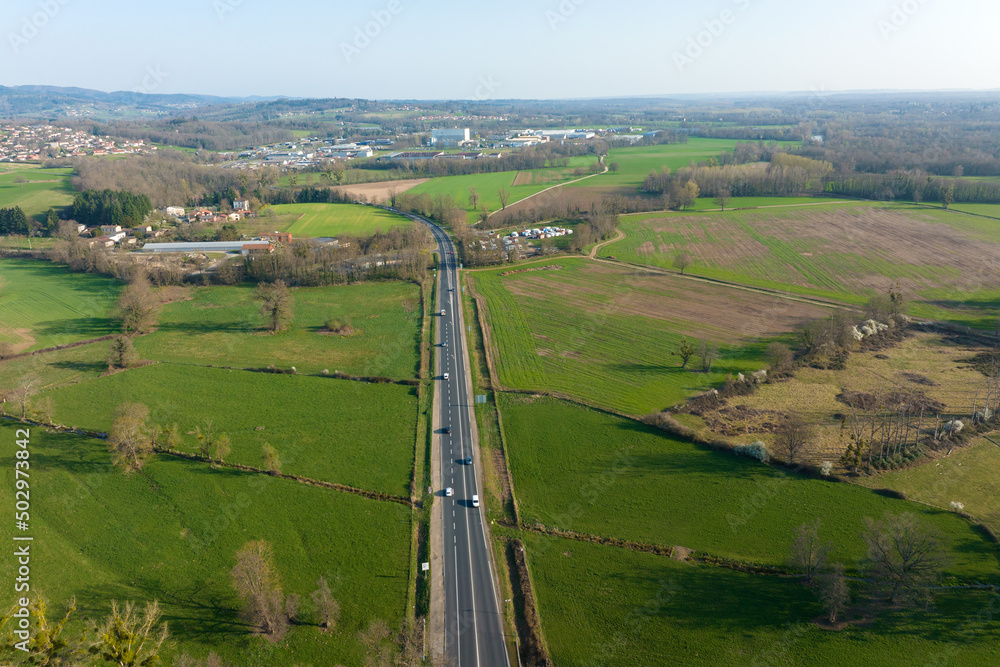 Aerial view of intercity road between green agricultural fields with fast driving cars. Top view from drone of highway traffic
