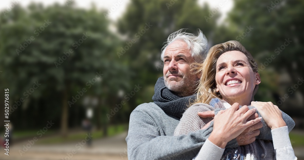 Fototapeta premium Smiling caucasian senior man embracing senior woman against trees in park during sunny day