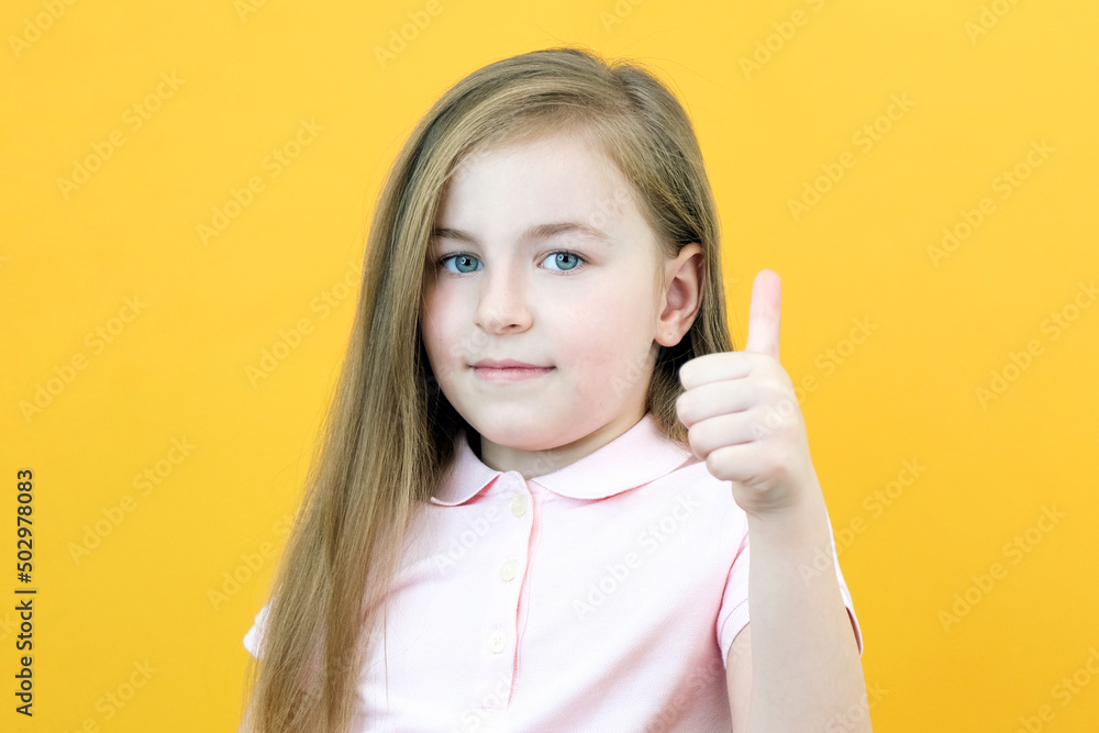 Portrait of an amazed cute girl pointing at an empty space in the background, a preschool girl shows a like on a yellow background Portrait of an amazed cute girl pointing at an empty space in the background, a preschool girl shows a like on a yellow background