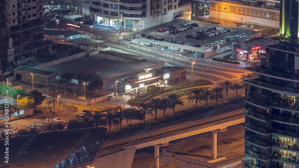 Futuristic buildings of Dubai with metro station and luxury skyscrapers behind near Dubai Marina night timelapse