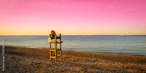 Pink sky at sunset at the beach with a lifeguard chair over the sandy shore