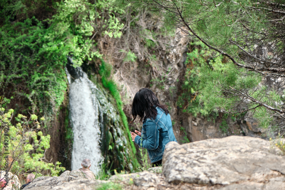 Waterfall behind the beautiful women background, woman looking to waterfall and wear denim jacket