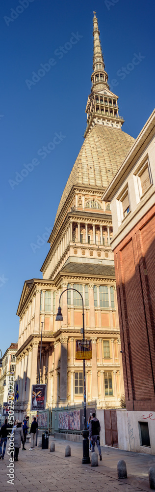 Turin, Italy. February 15, 2022. Vertical panoramic view of the Mole Antonelliana, home of the National Cinema Museum, taken from Via Montebello where some people are walking.