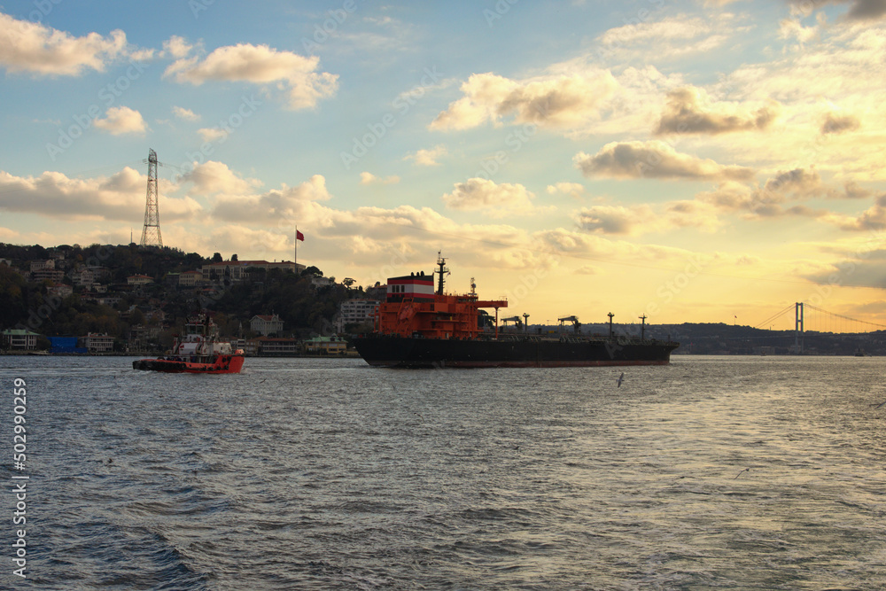 A cargo ship in the Bosphorus. Sea traffic in the Bosphorus. Different ships and boats are sailing on busy Bosphorus strait. Cityscape in the background, sky with white clouds during sunset. Istanbul