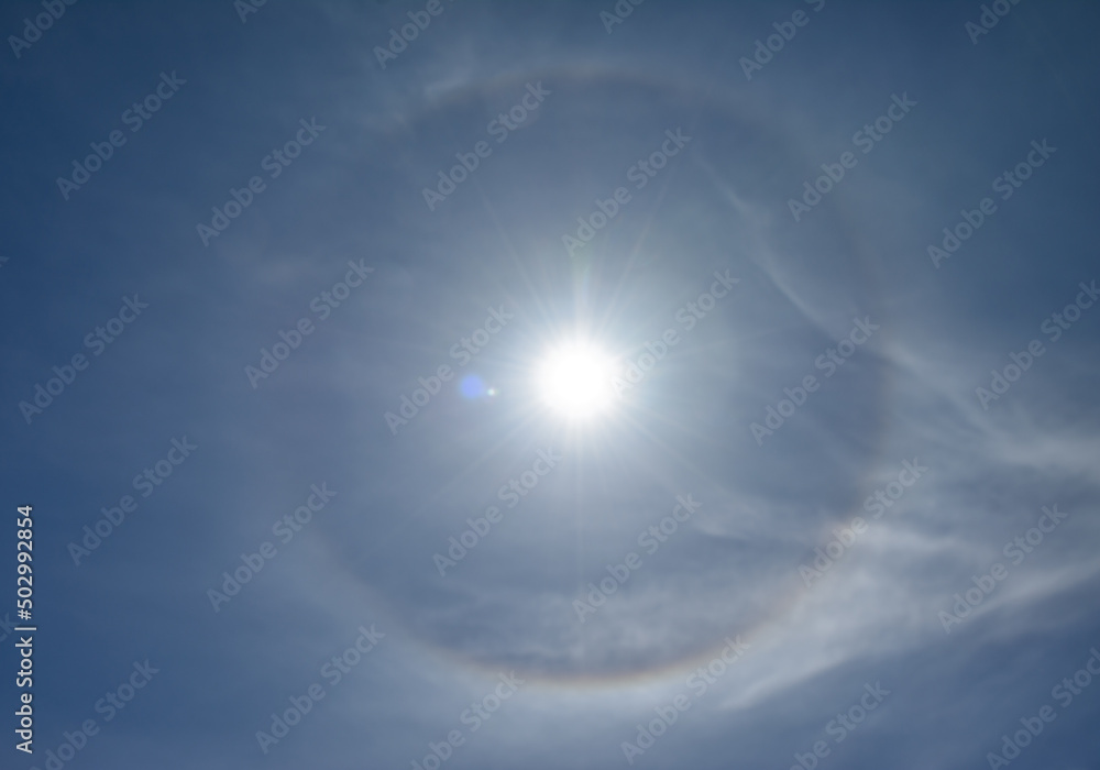 Optical phenomenon called 22 degree halo around the sun. Ice crystals in the atmosphere refract light and create the halo. Optical phenomenon called 22 degree halo around the sun. Ice crystals in the atmosphere refract light and create the halo.