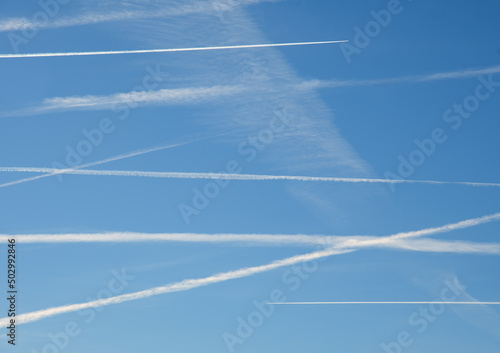 Several airplane contrails crossing the blue sky in a flyover state, with two planes actively making new trails on top and bottom, to opposite directions