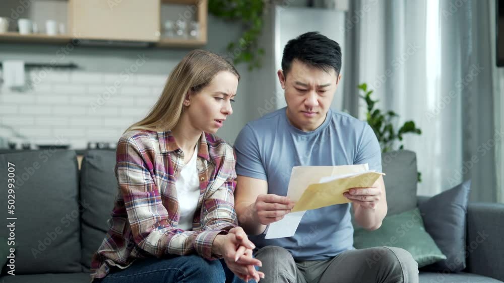 Upset Worried Multiracial couple, Asian man and woman, together at home, received a letter read with bad news, frustrated and sad sitting on the couch at home. unpaid bills and taxes feels stressed Upset Worried Multiracial couple, Asian man and woman, together at home, received a letter read with bad news, frustrated and sad sitting on the couch at home. unpaid bills and taxes feels stressed