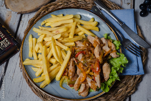 Chicken goulash with vegetables and french fries on a blue dish. Top view