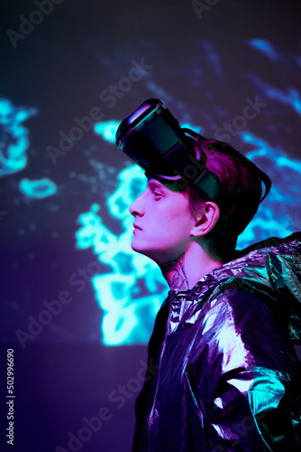 Side view of thoughtful young man in reflective jacket believing in new reality standing against neon background