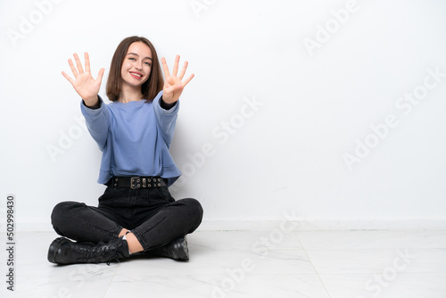 Young Ukrainian woman sitting on the floor isolated on white background counting nine with fingers