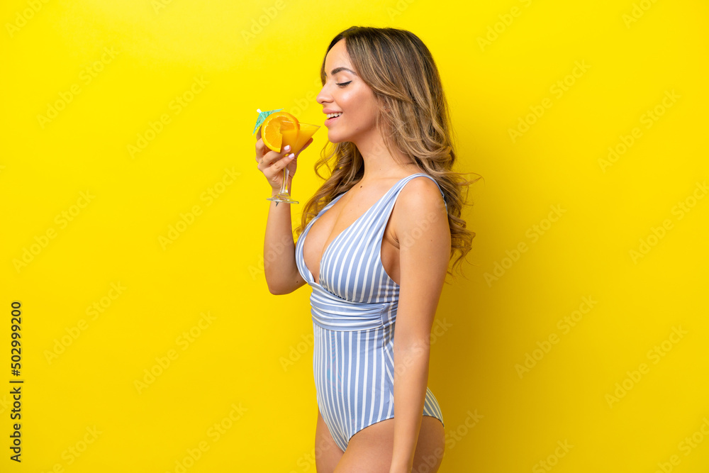 Young caucasian woman isolated on yellow background in swimsuit and holding a cocktail Young caucasian woman isolated on yellow background in swimsuit and holding a cocktail
