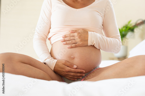 Mid section of caucasian pregnant woman touching her belly while sitting on the bed at home photo