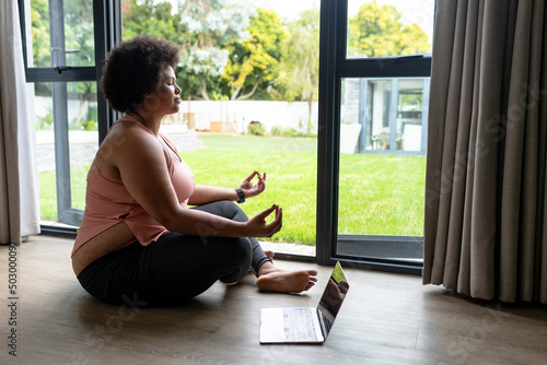 Side view of african american mid adult mediating while sitting by laptop at home entrance