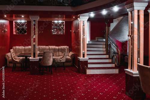 spiral staircase rises in the restaurant. the steps of the stairs are covered with a red carpet. columns with mirrors inside the restaurant. antique style.