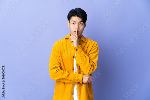 Young Chinese man isolated on purple background showing a sign of silence gesture putting finger in mouth