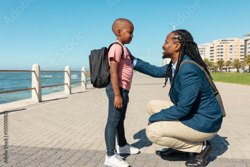 Obraz na plátně Smiling african american father crouching while talking to son with hand on shou