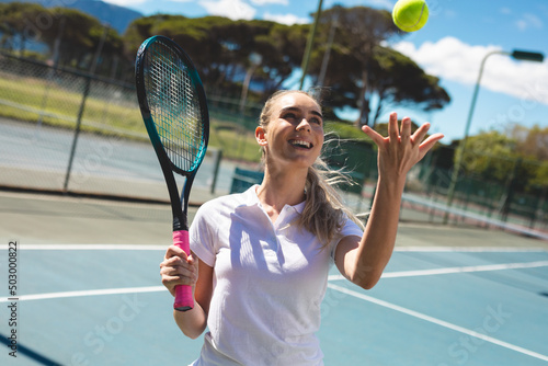 Cheerful young caucasian female player holding tennis racket while catching ball at court