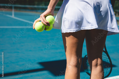 Rear view midsection of young female caucasian athlete holding tennis balls at court on sunny day