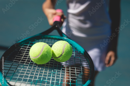 Tennis balls on racket held by young female caucasian player standing at court on sunny day