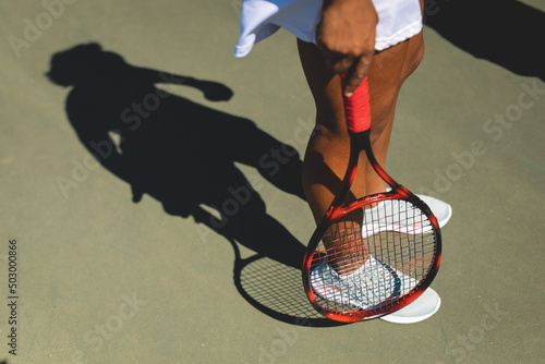 Low section of female african american player standing with tennis racket at court on sunny day