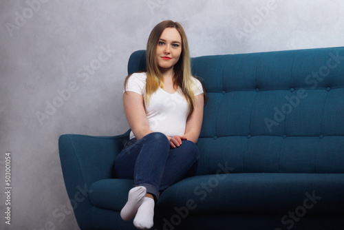Attractive young adult housewife woman sitting on the couch and looking at the camera in her house
