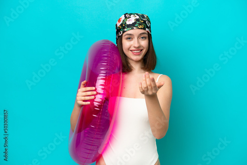 Young Ukrainian woman holding air mattress isolated on blue background inviting to come with hand. Happy that you came