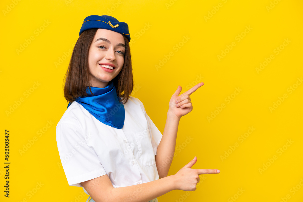 Airplane stewardess Ukrainian woman isolated on yellow background pointing finger to the side and presenting a product Airplane stewardess Ukrainian woman isolated on yellow background pointing finger to the side and presenting a product