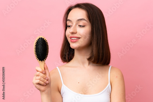 Young Ukrainian woman isolated on pink background with hair comb and looking it