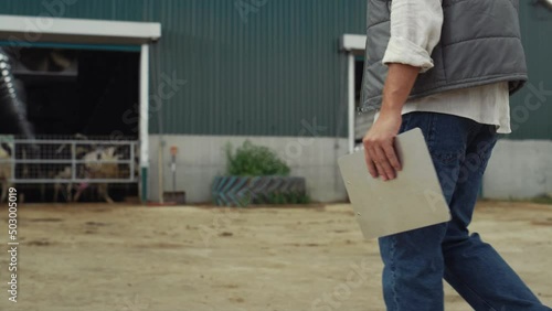 Farm worker walking livestock facility. Hand holding clipboard legs closeup. photo