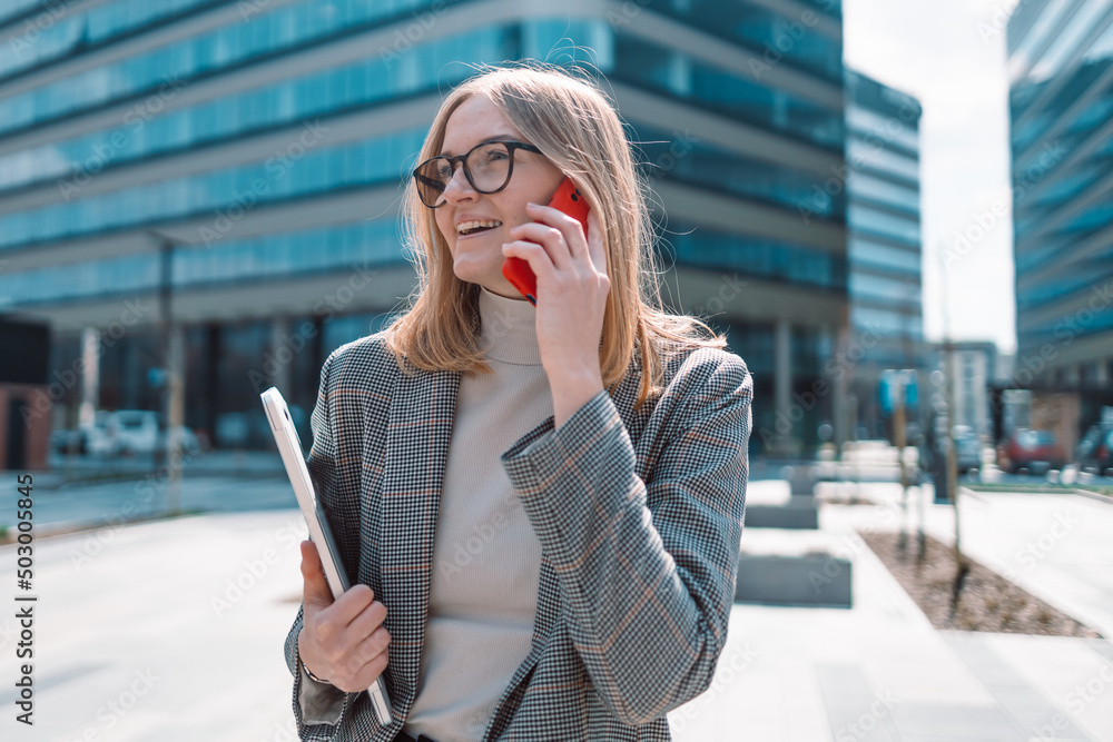 Fototapeta premium Closeup shot of confident 30s woman talking with somebody on mobile phone while walking in front of business center 