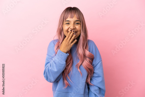 Young mixed race woman with pink hair isolated on pink background happy and smiling covering mouth with hand