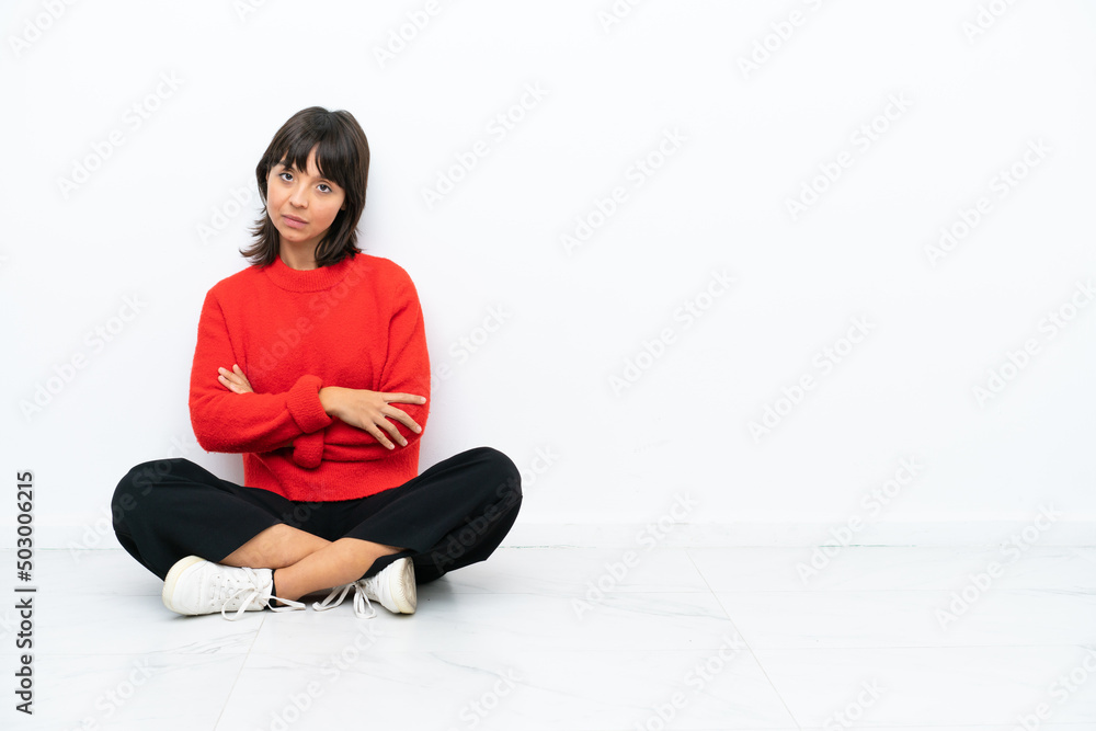 Young mixed race woman sitting on the floor isolated on white background with arms crossed and looking forward Young mixed race woman sitting on the floor isolated on white background with arms crossed and looking forward