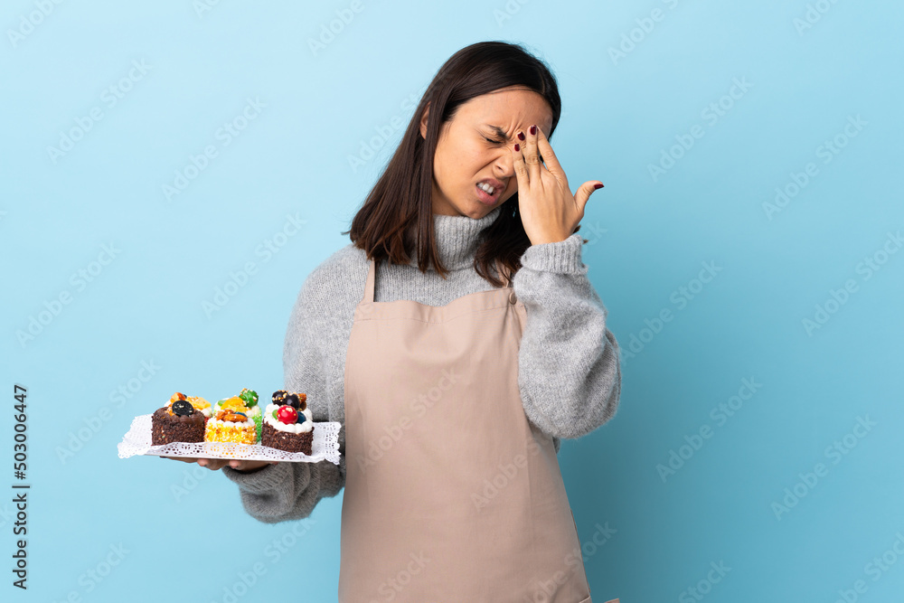 Pastry chef holding a big cake over isolated blue background with headache. Pastry chef holding a big cake over isolated blue background with headache.