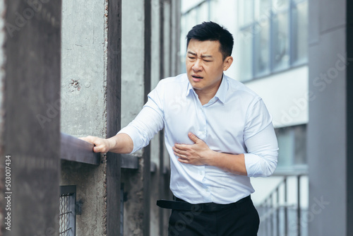 Vászonkép Asian office worker sick, having severe chest pain, businessman holding hands on