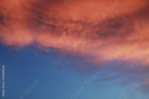 Dramatic sunset landscape with puffy clouds lit by orange setting sun and blue sky.