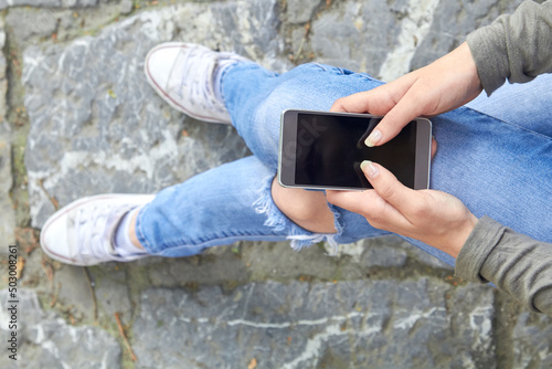 Woman in jeans using modern smartphone outdoors.