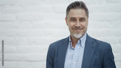 Middle age businessman in business casual. Entrepreneur in jacket. Mid adult, mature age man, happy smiling. Portrait against white brick wall with copy space.