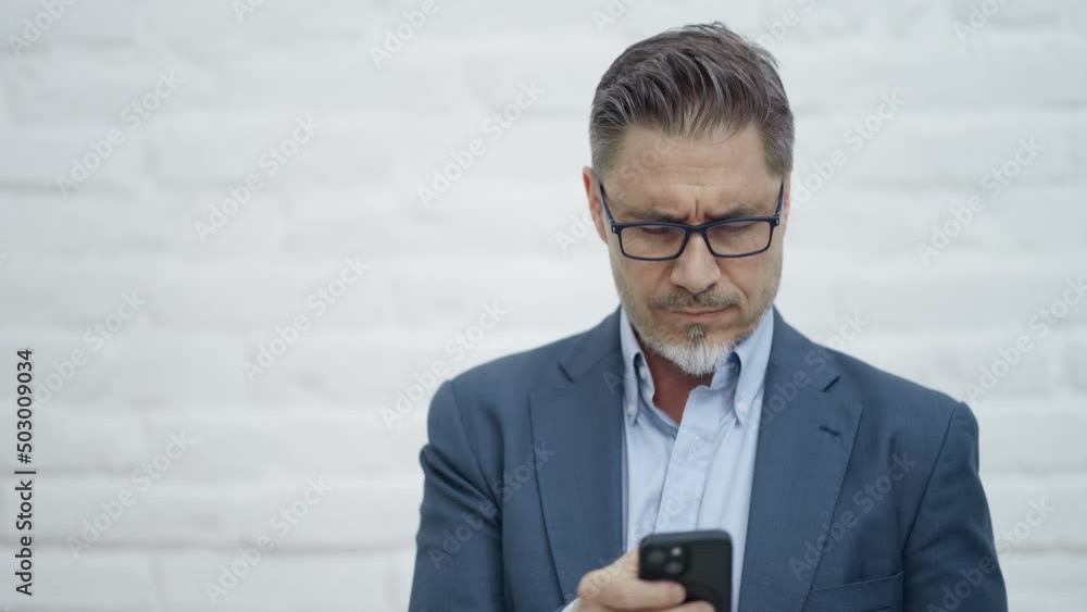 Middle age businessman with phone in business casual. Entrepreneur in jacket. Mid adult, mature age man, happy smiling. Portrait against white brick wall with copy space.