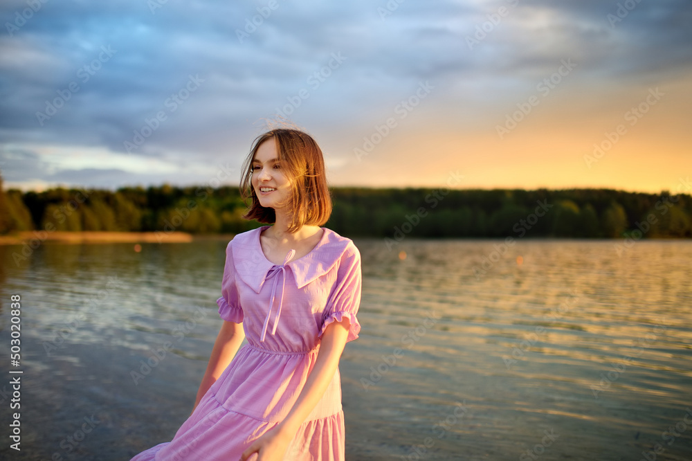 Beautiful teenage girl wearing pink dress having fun by a lake on warm and sunny summer day. Pretty young girl on a sunset. Beautiful teenage girl wearing pink dress having fun by a lake on warm and sunny summer day. Pretty young girl on a sunset.