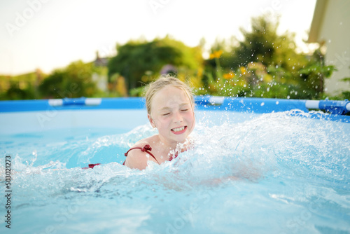 Cute young girl having fun in outdoor pool. Child learning to swim. Kid having fun with water toys. Family fun in a pool.