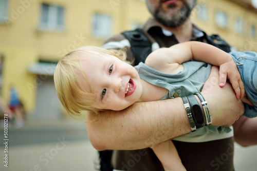 Cute toddler boy in his fathers arms. Dad and son having fun on sunny summer day in the city. Adorable baby being held by daddy.