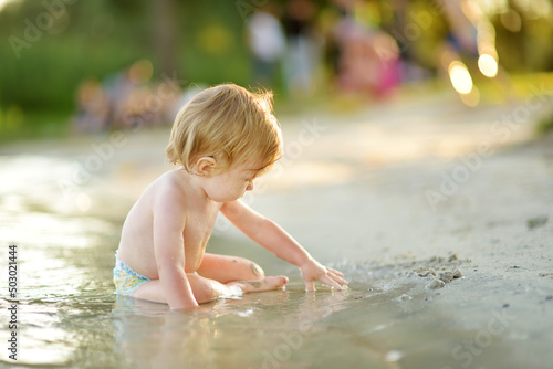 Cute toddler boy wearing swimming diaper playing by a river on hot summer day. Adorable child having fun outdoors during summer vacations.