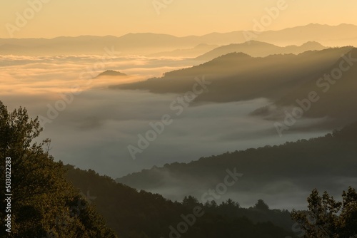 Golden sunrise at the summit of mountains above the clouds with fog and mist
