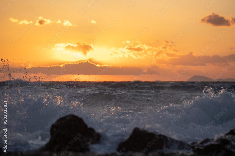 Sea ​​wave at sunset in gold hour hitting a rock on the beach.